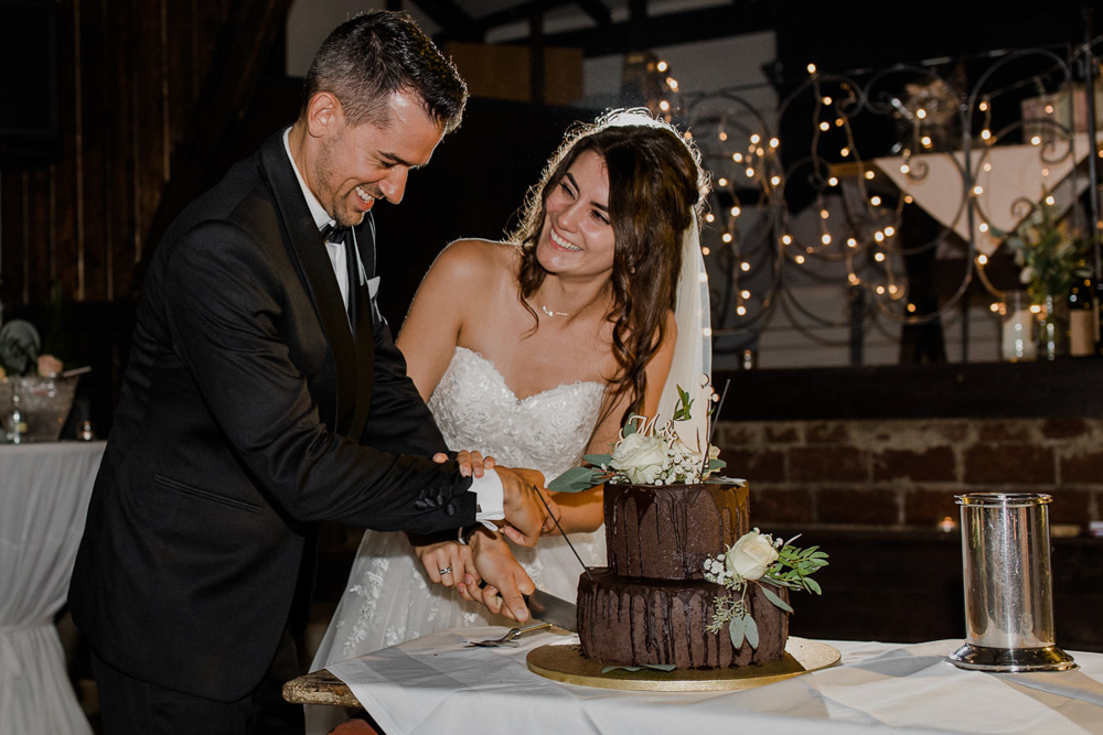 Brautpaar beim Hochzeitstortenanschnitt – glückliche Blicke und emotionale Momente während der Feier